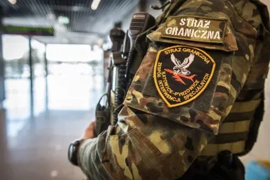 Funkcjonariusz polskiej Straży Granicznej w kamuflażu stoi wewnątrz budynku, na ramieniu widoczne naszywki oznaczające zespół interwencji specjalnych z Katowic-